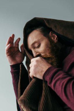 Kafasında kahverengi ceket olan sakallı adamın düşük açılı görüntüsü gri renkte izole edilmiş. 