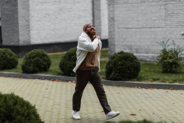 Şapkalı, modaya uygun güneş gözlüklü, modern binanın yakınında ceketli neşeli bir adam. 