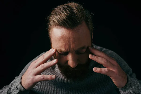 Stressed man in sweater touching head and closing eyes isolated on black