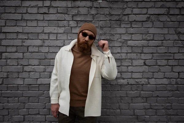 レンガの壁の近くに立っているビーニー帽子とサングラスのスタイリッシュな髭の男 — ストック写真