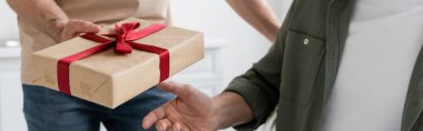 cropped view of man holding gift box with red ribbon near dad on fathers day, banner clipart