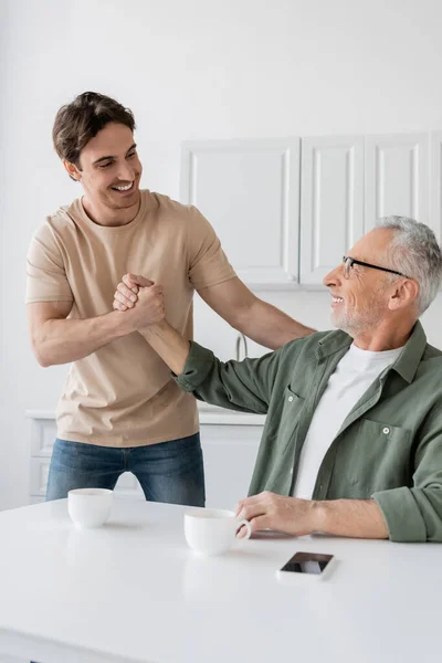 stock image happy dad and son shaking hands near coffee cups and mobile phone with blank screen on kitchen table