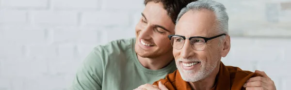 stock image cheerful young man with closed eyes hugging bearded and mature father in eyeglasses, banner