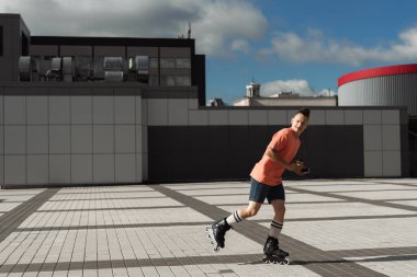 Young man in roller skates holding coffee to go and smartphone while riding on urban street  clipart