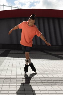 Young man in roller skates riding on urban street at daytime  clipart