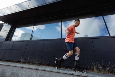 Side view of man in roller blades doing trick on parapet on urban street  clipart