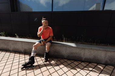 Patenli gülümseyen adam kulaklık takıyor ve elinde kağıt bardak tutuyor. 