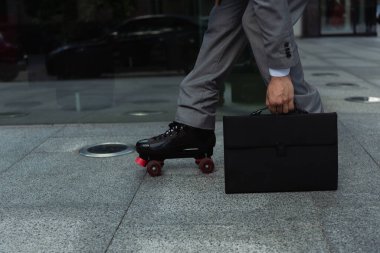 cropped view of roller skater in formal wear holding black briefcase on street clipart