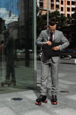 Resmi giyimli ve paten giyen şık bir adam şehir caddesinde evrak çantasını kapatıyor.