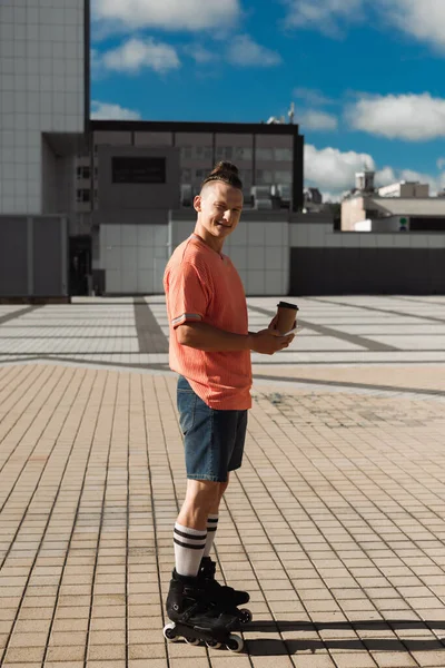 Ung Rullskridskoåkare Håller Smartphone Och Kaffe För Att Medan Tittar — Stockfoto