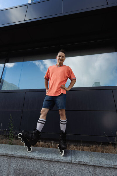 Wide angle view of smiling man in roller blades standing on parapet outdoors 