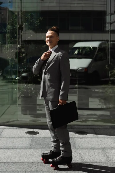 Mosolygós Üzletember Öltönyben Görkorcsolyával Rögzítő Nyakkendő Kamera Közelében Üveg Homlokzat — Stock Fotó