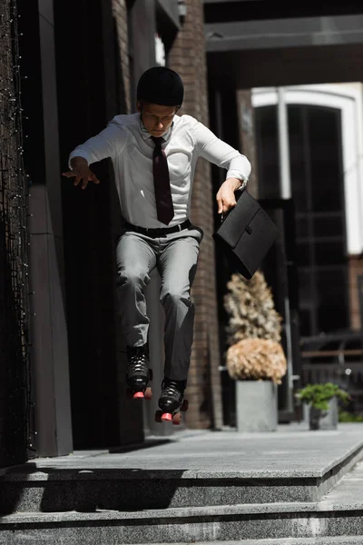 ローラースケートやヘルメット保持ブリーフケースのビジネスマン街の通りの階段からジャンプしながら — ストック写真