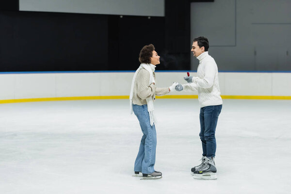 Side view of man doing propose to african american girlfriend on ice rink 