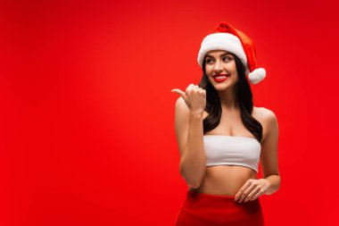 Noel Baba şapkalı gülümseyen kadın kırmızıda izole edilmiş bir parmakla işaret ediyor.