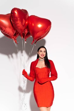 Beyaz arka planda kırmızı kalp şeklinde balonlar tutan neşeli esmer kadın. 