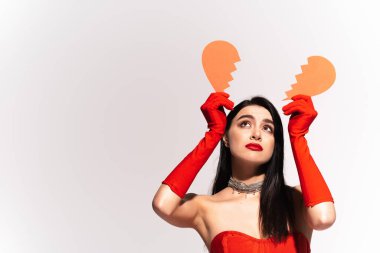Kırık kalbi gri renkte olan kırmızı eldivenli üzgün bir model. 