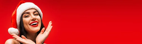 Szczęśliwy Młody Model Kapeluszu Mikołaja Patrząc Kamerę Odizolowaną Czerwono Przestrzenią — Zdjęcie stockowe