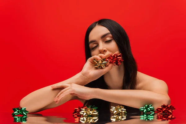 Young woman with naked shoulder holding gift bows isolated on red