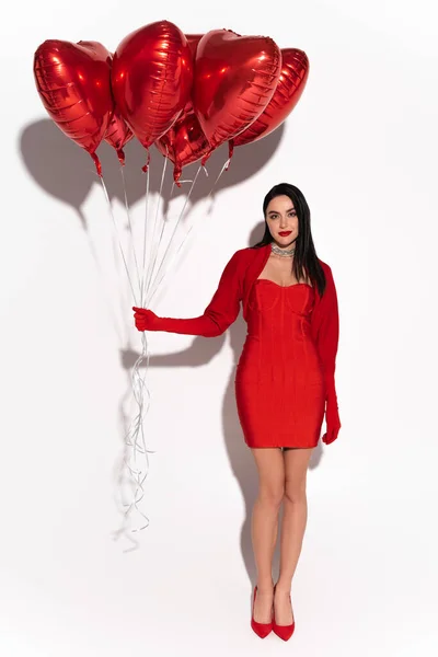 stock image Full length of stylish woman in red dress and heels holding heart shaped balloons on white background with shadow 