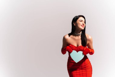 Kırmızı elbiseli, çıplak omuzlu, kağıt kalpli neşeli bir kadın. 