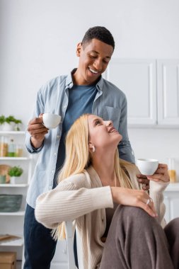 Neşeli ırklar arası çift sabah kahvesi içip mutfakta birbirlerine gülümsüyorlar.