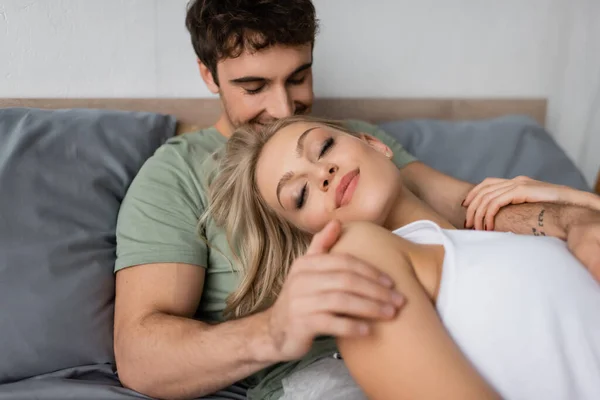 Man in pajama touching blonde girlfriend with closed eyes on bed