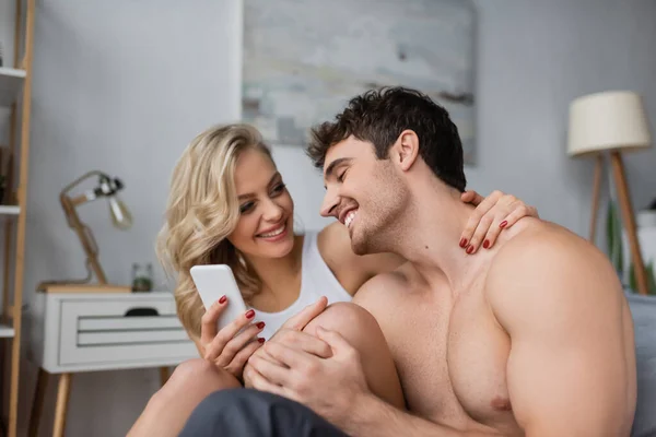Gülümseyen Sarışın Kadın Akıllı Telefon Tutuyor Yatak Odasında Üstsüz Erkek — Stok fotoğraf