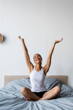 smiling african american woman stretching while sitting on bed in morning  clipart
