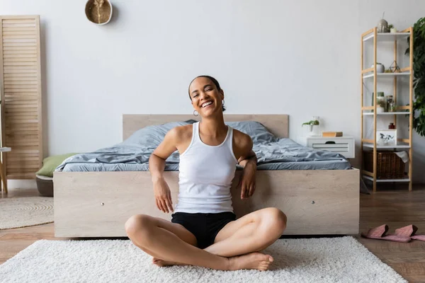 Νέα Και Χαρούμενη Αφροαμερικανή Μπλουζάκι Που Κάθεται Κοντά Στο Κρεβάτι — Φωτογραφία Αρχείου