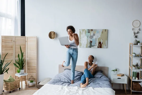 Excited African American Lesbian Woman Holding Laptop While Standing Bed — Stock Photo, Image