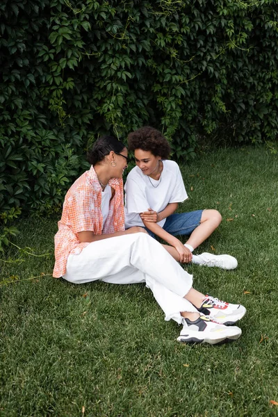笑顔アフリカ系アメリカ人レズビアン女性ですサングラスで幸せな彼女を見ながら芝生の上に座って — ストック写真