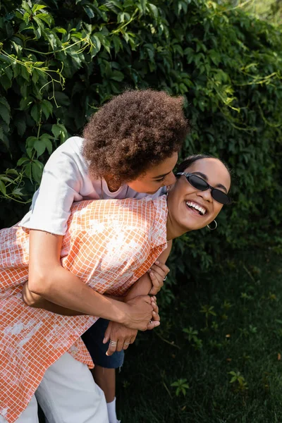 快乐的非洲裔美国女同性恋者 戴着时髦太阳镜拥抱着快乐的女朋友 在公园里大笑 — 图库照片