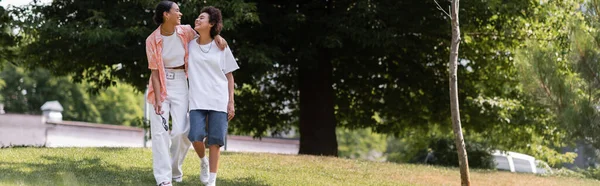 若いアフリカ系アメリカ人女性がレズビアンパートナーを抱きかかえて緑の公園を歩き — ストック写真