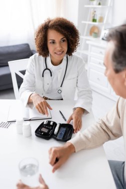Gülümseyen Afrikalı Amerikalı doktor diyabeti olan orta yaşlı bir adama bakıyor. 