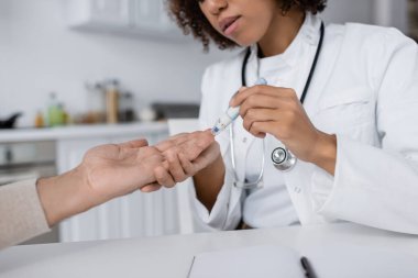 cropped view of curly african american doctor taking blood sample of middle aged man with lancet pen clipart
