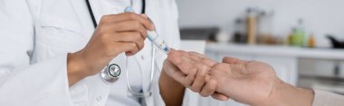 Afro-Amerikan doktorların orta yaşlı bir adamın pankart ve tükenmez kalemle kan örneğini aldığına dair kısmi görüş. 