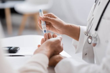 Steteskoplu Afrikalı Amerikalı bir doktorun klinikte diyabeti olan bir hastadan kan örneği alması. 
