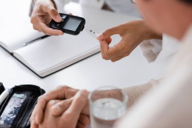 Afrika kökenli Amerikalı doktorun elinde glukometre cihazı ve test şeridi tutarken orta yaşlı bir hastaya baktığını gördüm.