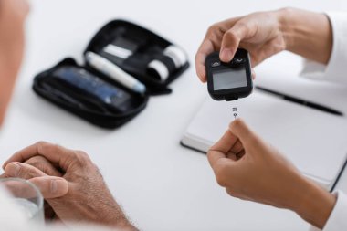 Afrikalı Amerikalı doktorun orta yaşlı hastaya glucometre cihazı ve test bandı göstermesi