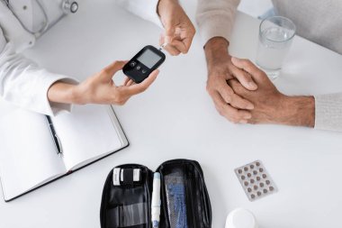 top view of african american doctor showing glucometer device and test strip to middle aged patient clipart