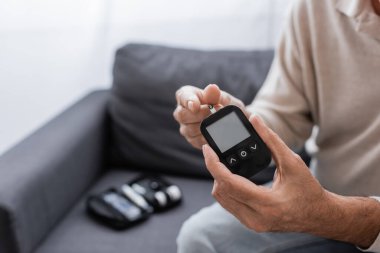 Glikoz ölçer cihazı ve test şeridi tutan orta yaşlı bir adamın kısmi görüntüsü