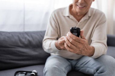 Glikoz ölçer cihazı tutan orta yaşlı, neşeli bir adamın kısmi görüntüsü 