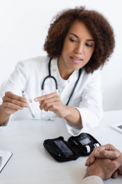Afro-Amerikalı doktor klinikte diyabeti olan orta yaşlı bir hastanın yanındaki tükenmez kalemi işaret ediyor.