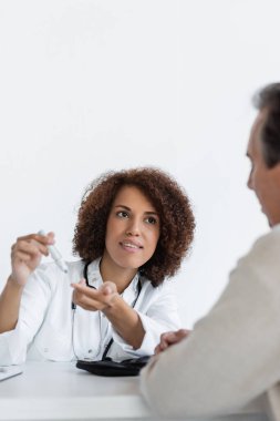 Neşe saçan Afrikalı Amerikalı doktor klinikte diyabeti olan orta yaşlı bir hastanın yanındaki tükenmez kalemi işaret ediyor.