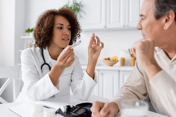 stock image curly african american doctor explaining how to use lancet pen to middle aged patient with diabetes