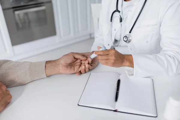 stock image cropped view of african american doctor taking blood sample of middle aged man with lancet pen