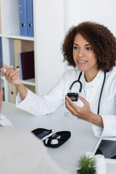 stock image cheerful african american doctor holding glucometer and talking with middle aged patient with diabetes