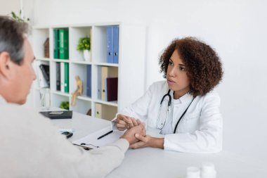 Afro-Amerikalı doktor diyabetli hastaların ellerini kontrol ediyor ve klinikte konuşuyor. 