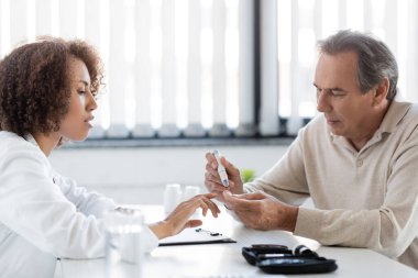 Afrikalı Amerikalı doktor klinikte eski bir hastaya neşter kalem kullanarak bakıyor. 